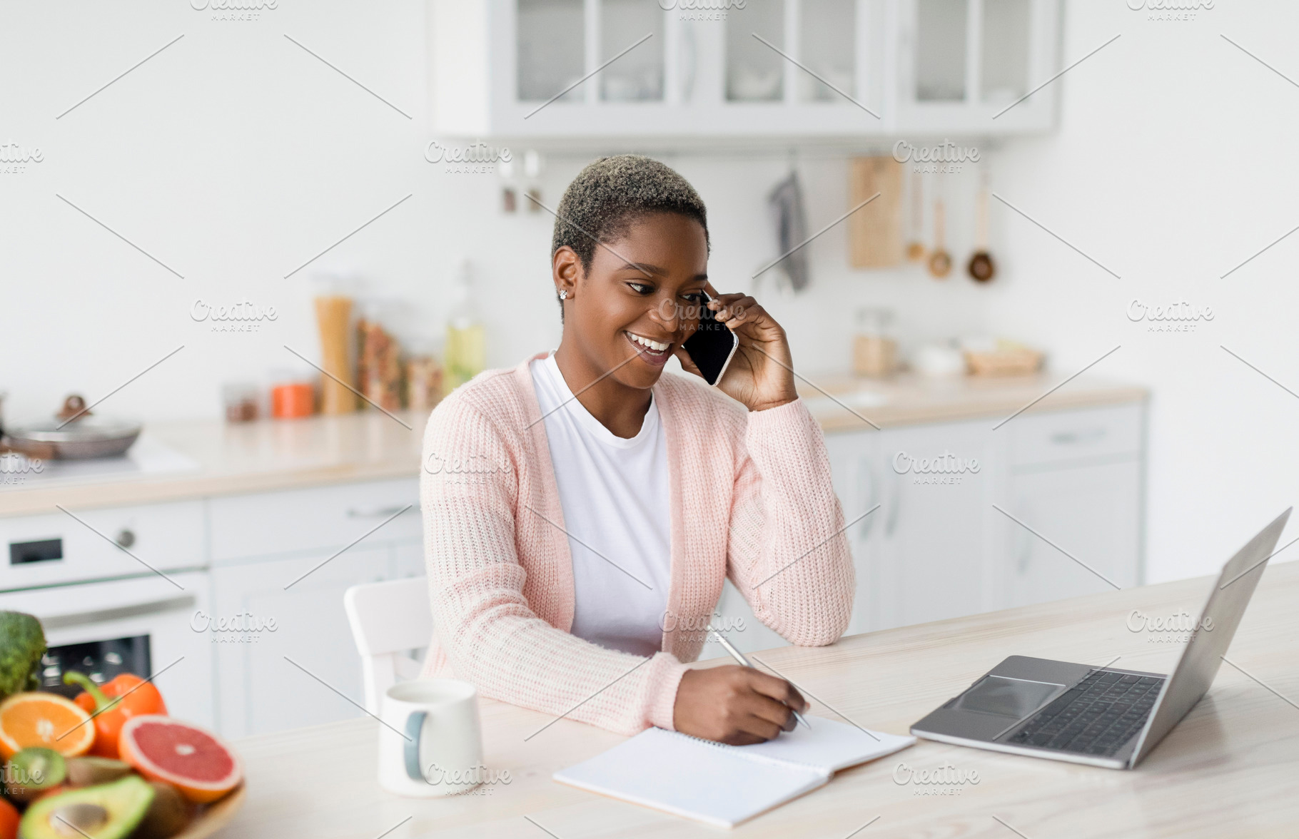 Smiling millennial pretty black lady manager speaks by phone and looks at lapto, a Person Photo by Prostock-Studio