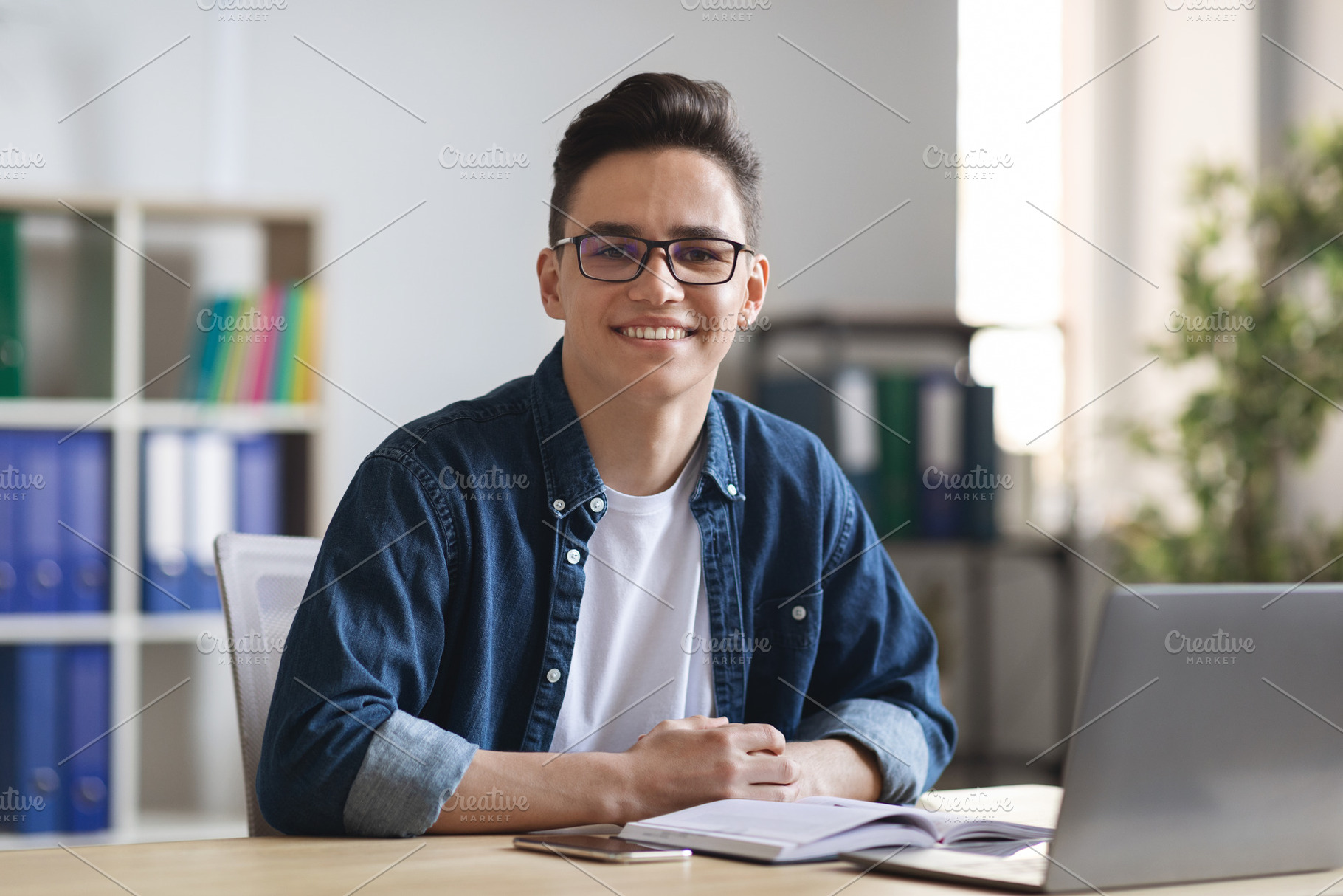 Smiling Young Male Entrepreneur Sitting At Desk With Laptop In Modern Office, a Photo by Prostock-Studio