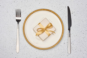A gift with a gold bow on a white plate next to a fork and knife, a Holiday Photo by ndanko