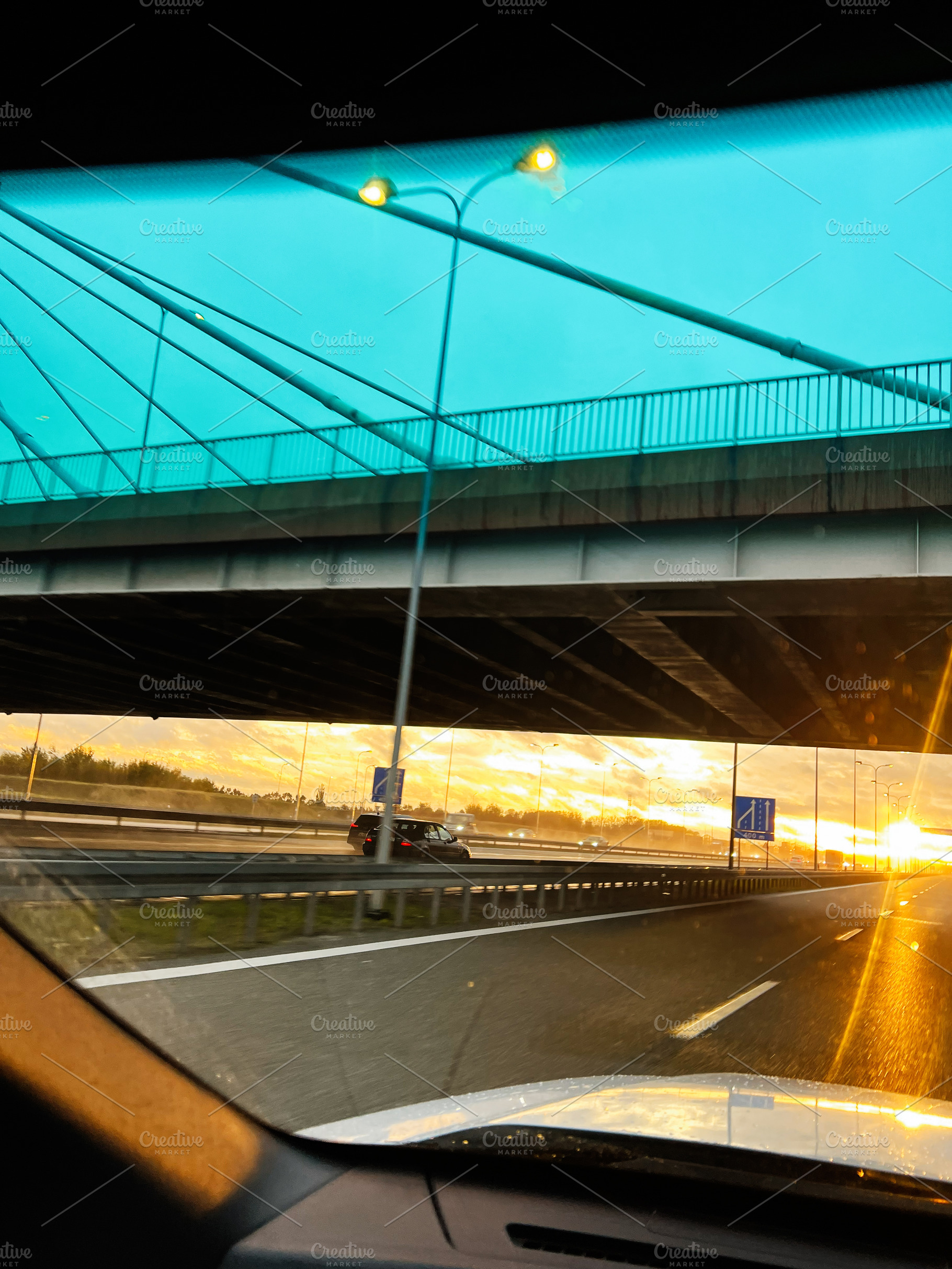Vehicles on a highway at sunrise viewed from inside a car under a turquoise bri, a Photo by AS photostudio
