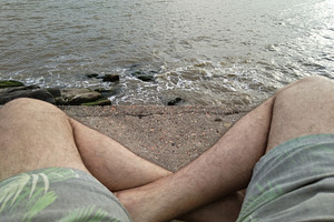 Person sitting by water with legs visible and  shorts, a Person Photo by DanFLCreativo
