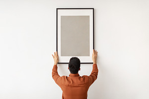 Young man hanging picture frame on the wall, a Photo by Prostock-Studio
