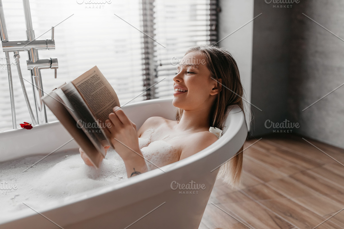 Happy woman lying in foamy bath, reading book in relaxing atmosphere, enjoying, a Photo by Prostock-Studio (Photo 2 of 2)