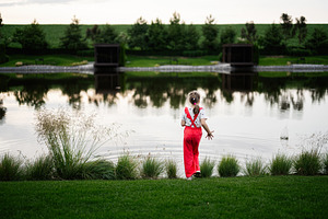 Young girl in red pants gazing at a serene pond in the evening, a Photo by AS photostudio