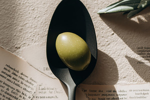 Black Spoon Holding a Single Olive, a Photo by Virgo Studio