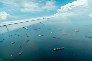Airplane arriving over sea with cargo ships in Singapore, a Transportation Photo by GoodGoods