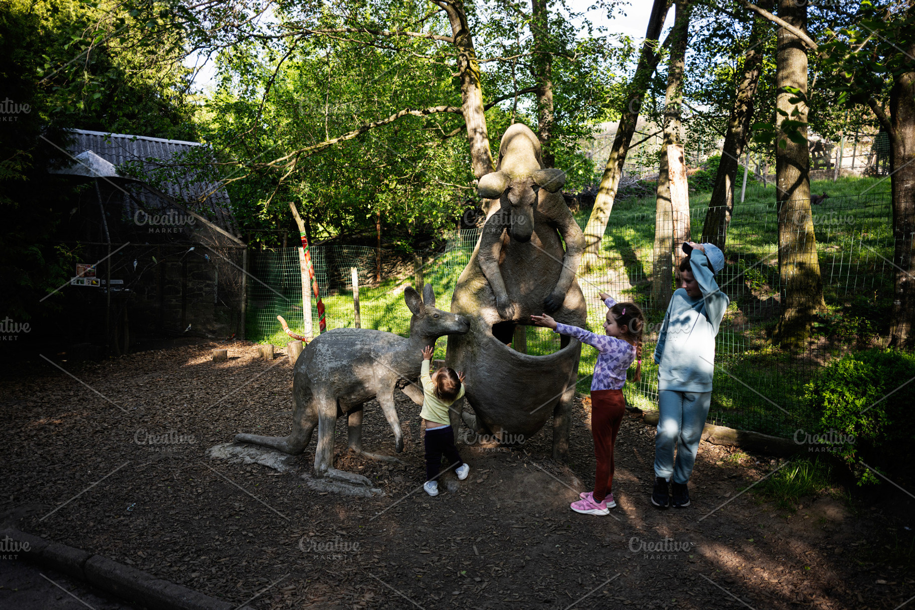 Children interacting with kangaroo statues in a lush outdoor park setting, a Photo by AS photostudio