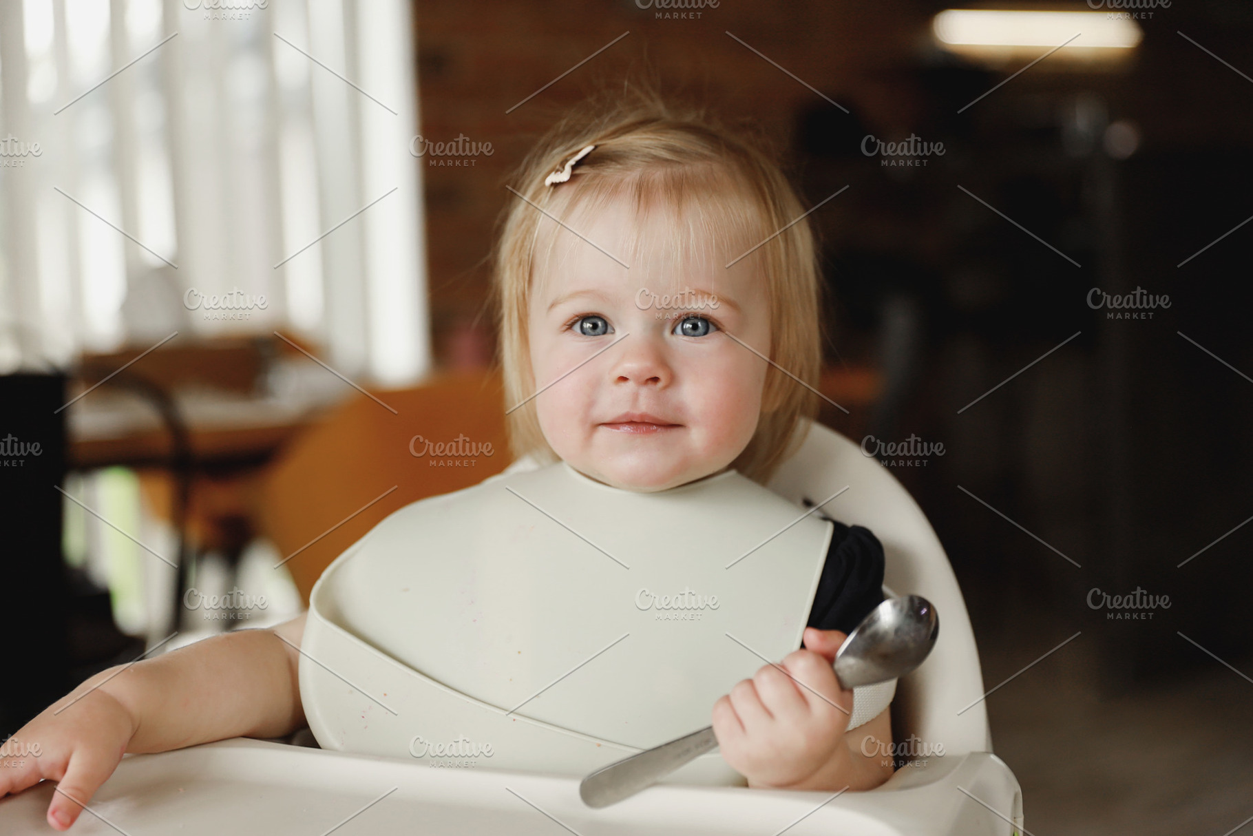 Infant girl or toddler sitting on high chair. Eating food by herself using spoo, a Person Photo by Lenor4ik