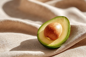 Fresh half of a ripe avocado on a beige linen fabric laid on a wooden table, a Food & Drink Photo by AlyaAnd