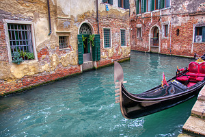 Gondola sailing through a canal in v containing venice, gondola, and famous