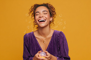 Joyful woman smiling brightly while holding a decorative ball against a vibrant, a Photo by AlyaAnd