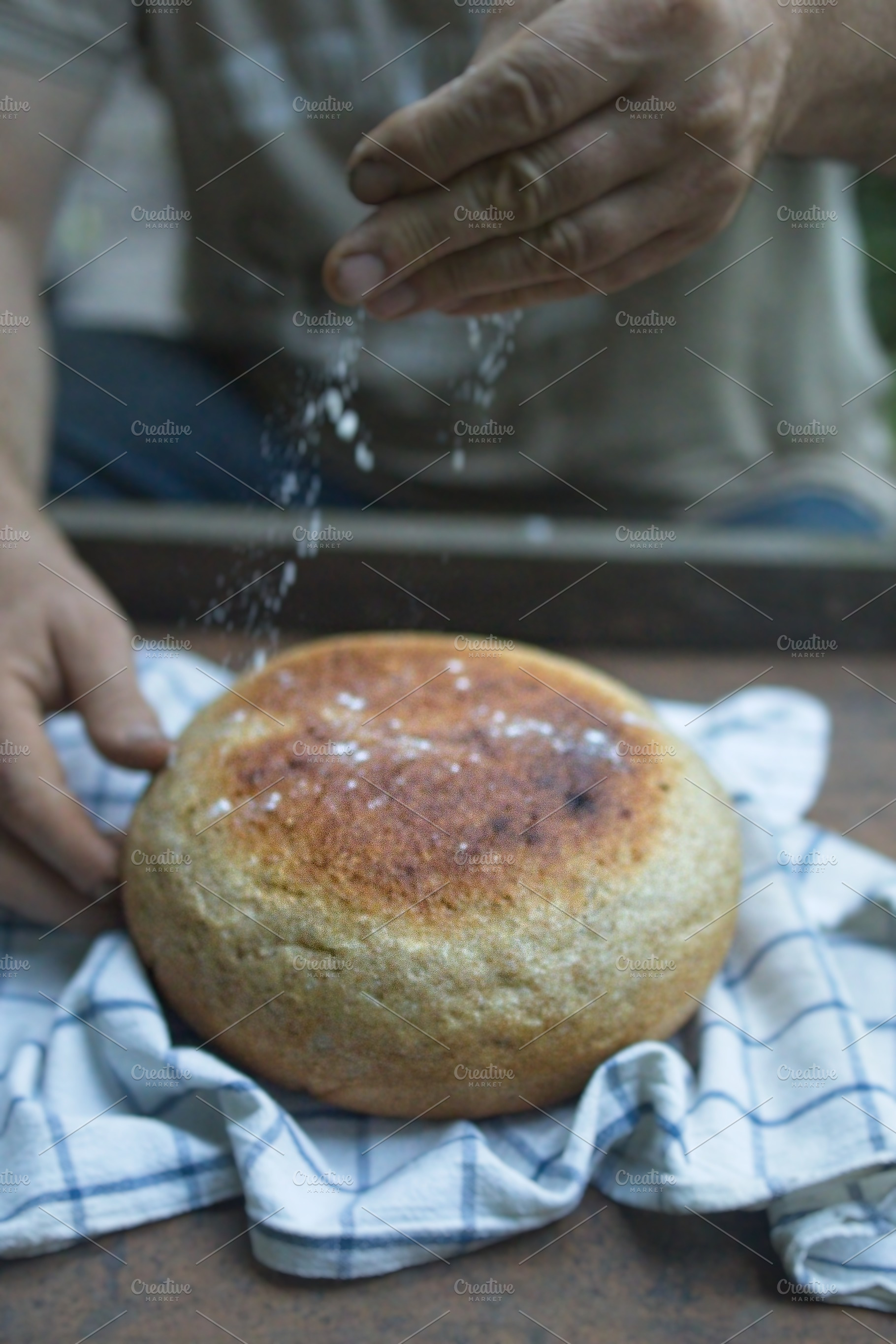 Baker's hand sprinkles flour on fresh bread close-up. A man finishes baking, de, a Food & Drink Photo by TanaCh