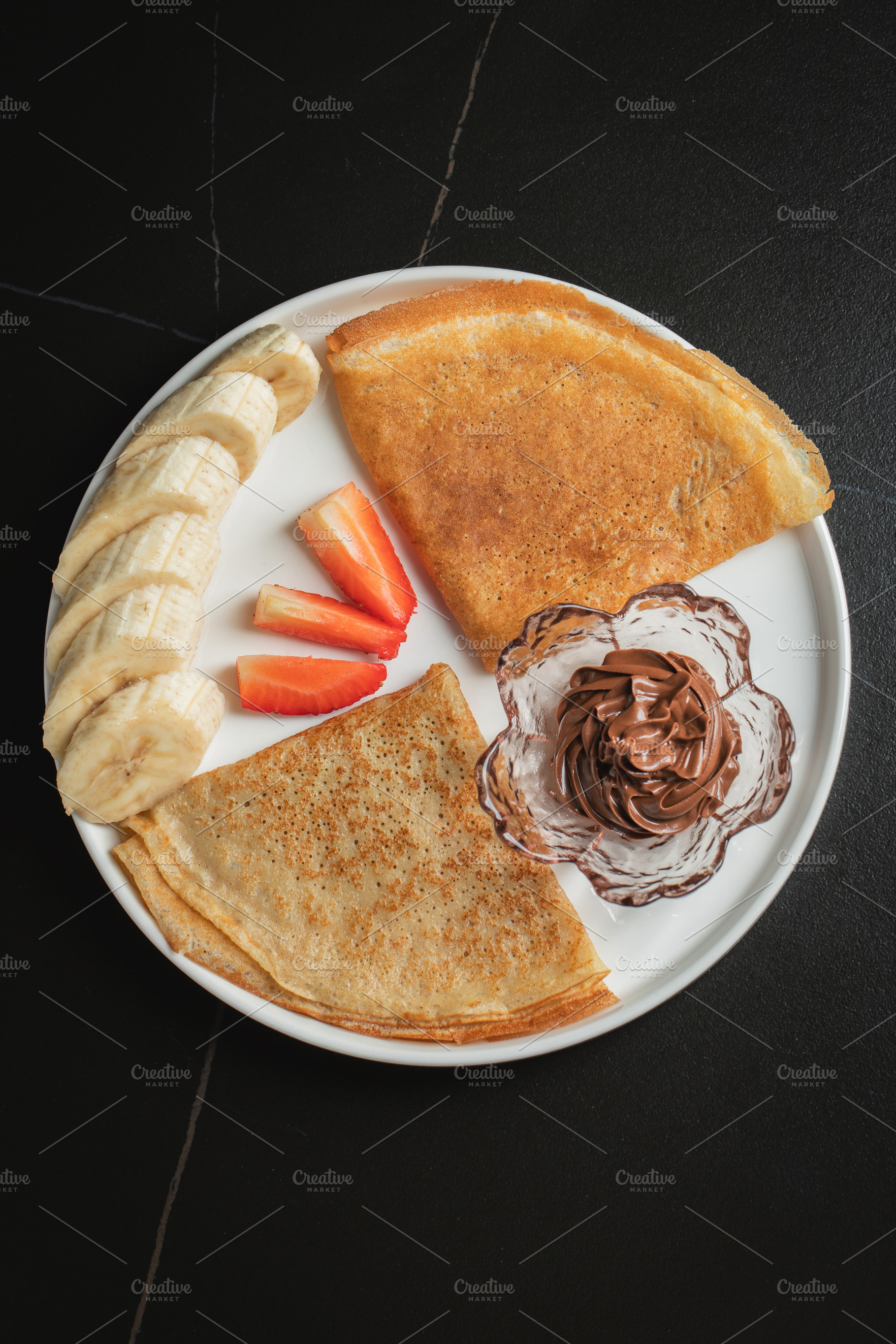 A plate of crepes filled with chocolate spread and topped with b, a Food & Drink Photo by Budarinphoto