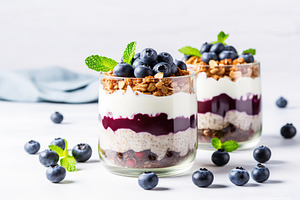 Chia pudding with blueberry and granola in glass on white background, a Food & Drink Photo by AlyaAnd