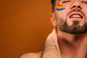 Young man expressing pride with rainbow face paint, a Photo by karrastock
