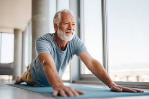 Elderly man practicing yoga in a bright room, a Person Photo by AlyaAnd