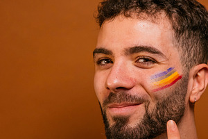 Young man smiling at camera with rainbow face paint, a Photo by karrastock