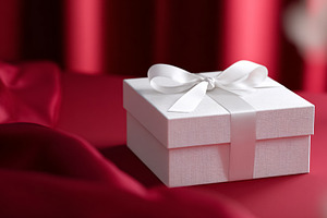White gift box with ribbon on lush red satin, symbolizing Valent, a Photo by Studio ANNA