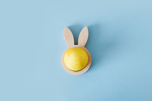 Happy Easter! Modern yellow easter egg in wooden bunny ears hold, a Holiday Photo by Sonjachni