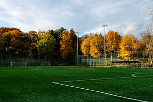 Autumn football field under blue sky with colorful trees and empty pitch, a Photo by AS photostudio