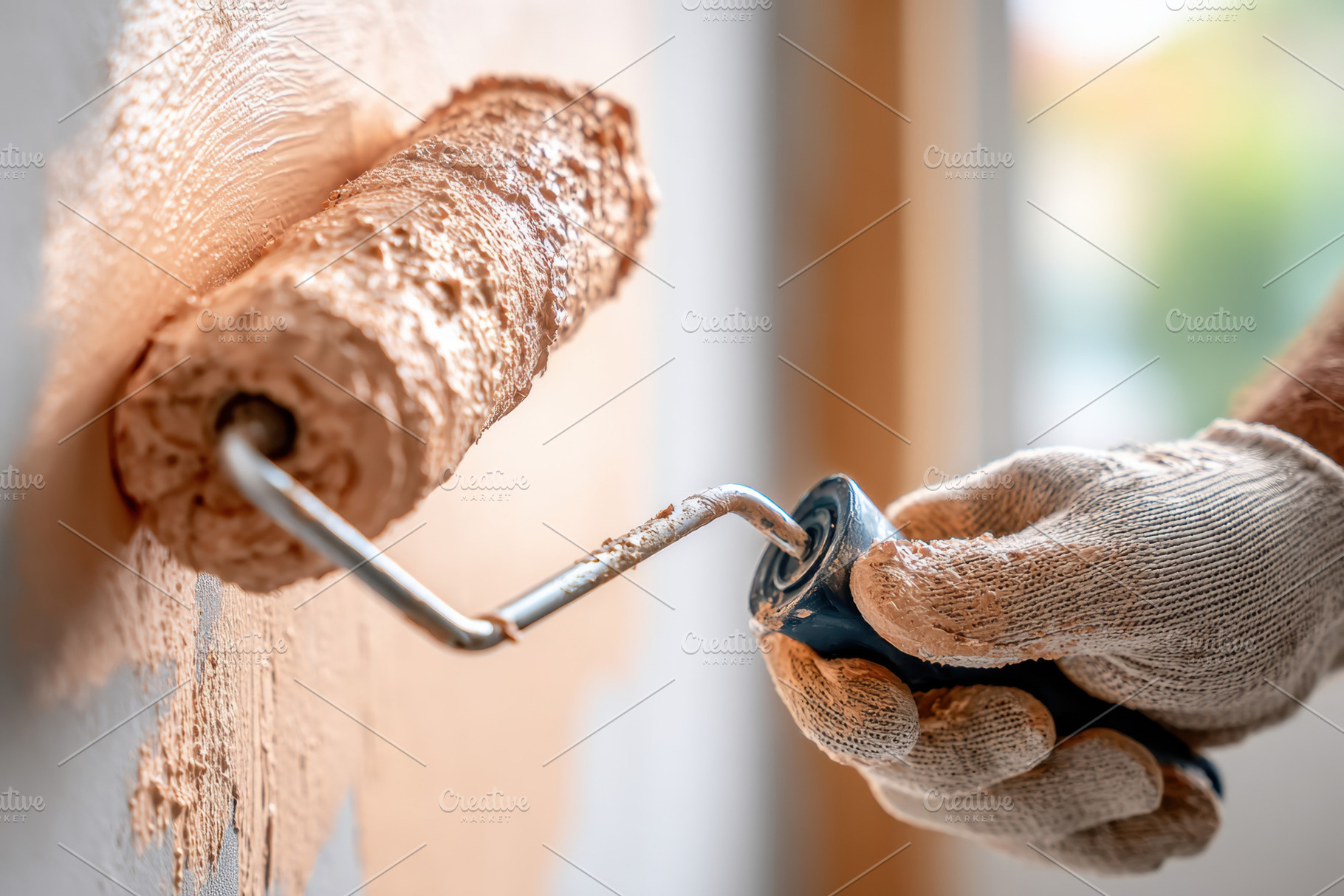 Hand applying paint with roller on wall in a room during daylight hours, an Industrial Photo by AlyaAnd