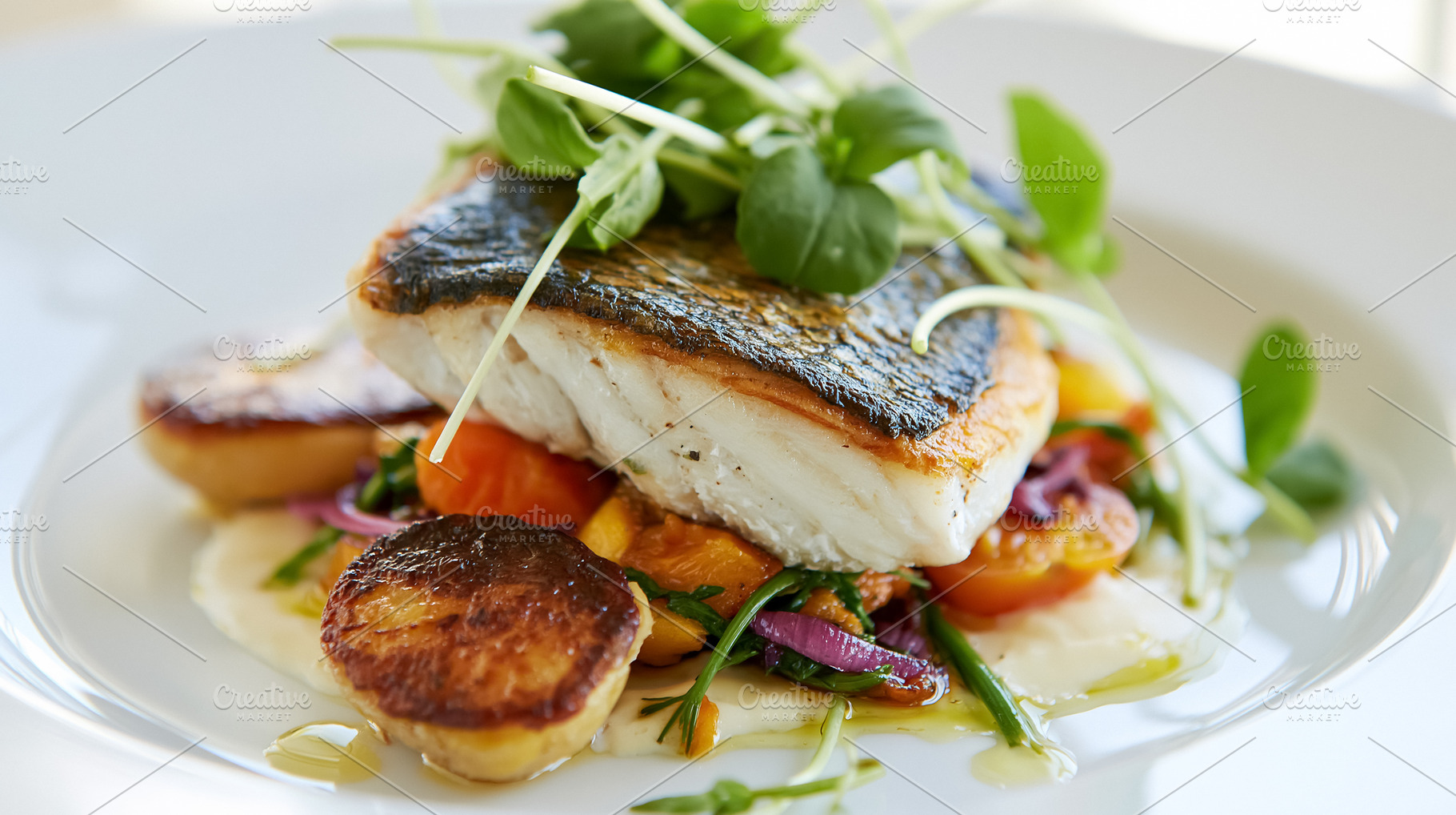 Seared sea bass fillet on a bed of roasted vegetables and scallops, garnished w, a Photo by Studio ANNA
