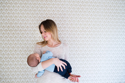 Beautiful mother holding baby son in her arms against wall, a Person Photo by HalfPoint