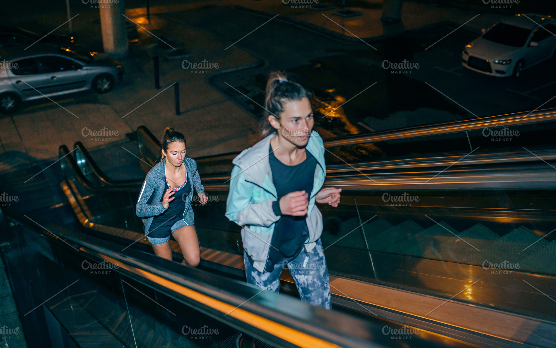 Women friends training running up escalator in city at night, a Sports & Recreation Photo by davidpereiras
