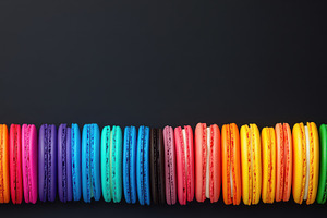 Brightly colored macarons arranged in a row against a black background, highlig, a Food & Drink Photo by Mashimara