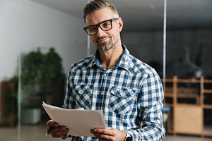 Joyful white-haired man working with papers while standing in office