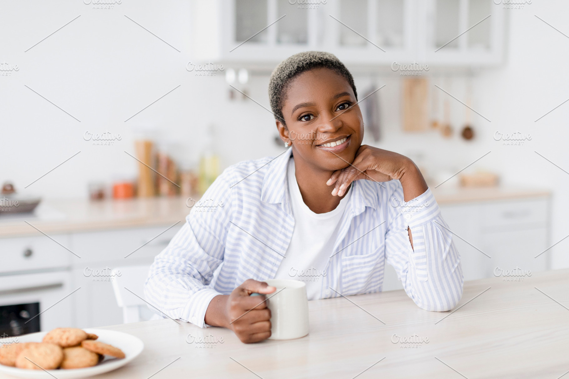 Glad happy millennial pretty black female with cup of favorite drink sits at ta, a Person Photo by Prostock-Studio