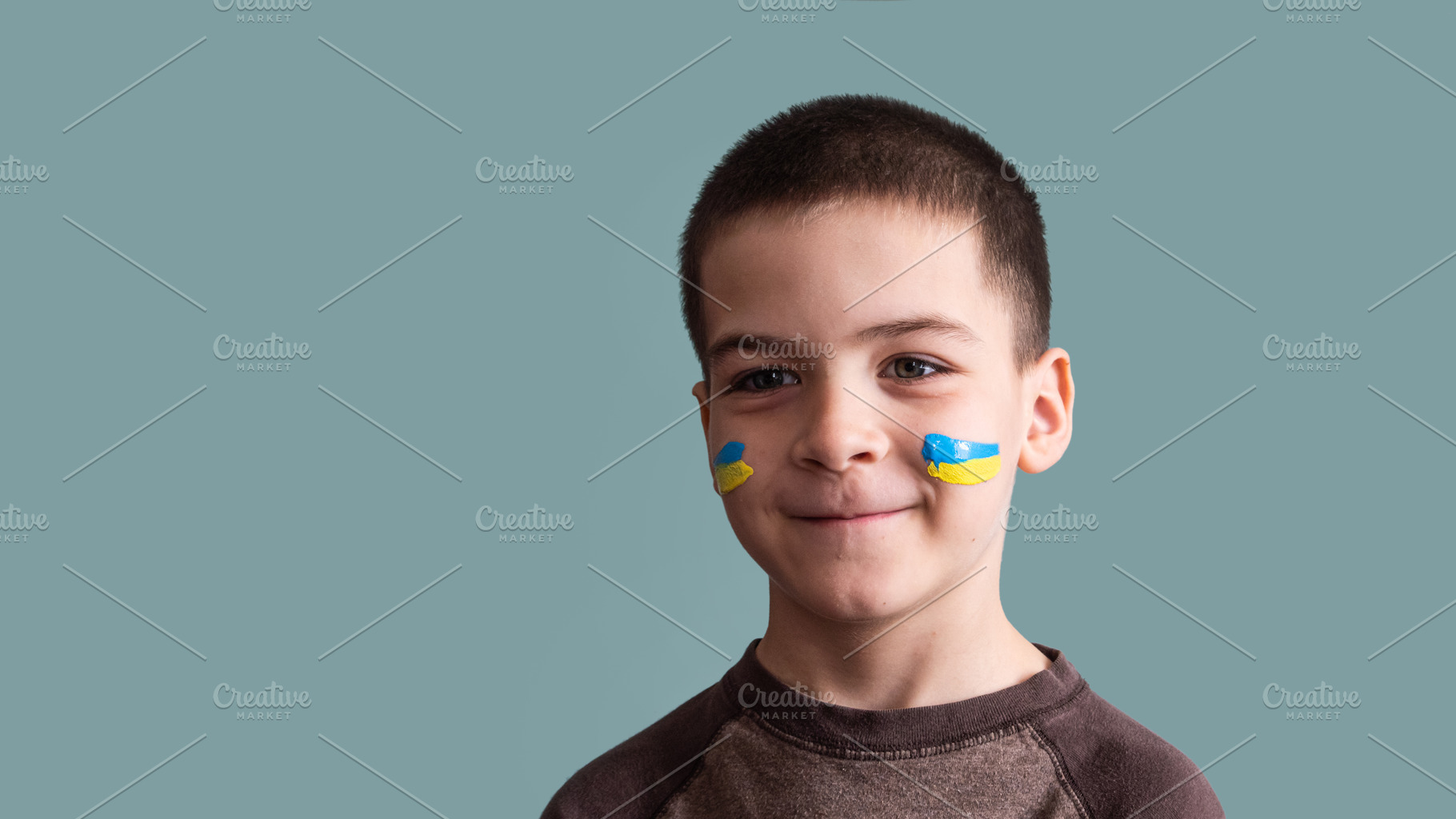 Child against war. Upset Ukrainian boy with bue yellow flag on his face, a Photo by OleksandrRybitskyi