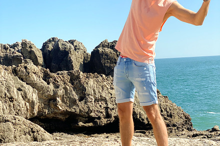 Man in casual summer attire posing playfully on rocky coastal te