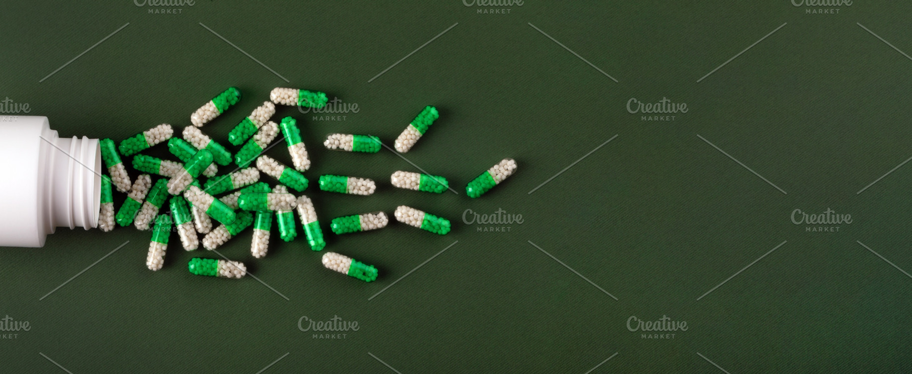White and green medicine capsules spill from a bottle onto a textured green sur, a Health & Medical Photo by Ales Munt