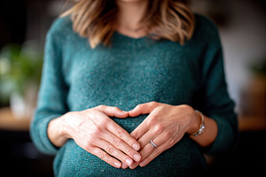 Pregnant woman gently cradling her baby bump with both hands indoors, a Person Photo by AlyaAnd