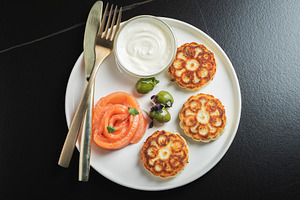 Savory Syrniki with Smoked Salmon, Olives and Sour Cream on White Plate