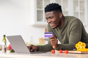Ordering Food Online. Black Guy Using Laptop And Credit Card In Kitchen, a Photo by Prostock-Studio