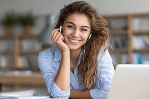 Smiling woman enjoys a video call while sitting at a laptop in a bright workspa, a Person Photo by AlyaAnd