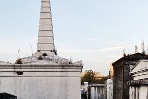 Obelisk tomb in a quiet New Orleans cemetery under a clear blue sky, a Photo by AS photostudio