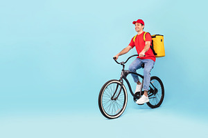 Courier Man With Backpack Riding Bike Delivering Food, Blue Background, a Photo by Prostock-Studio