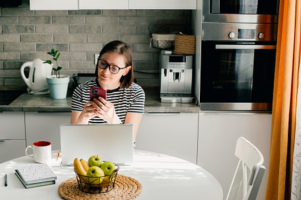 Freelancer woman wearing glasses using phone and laptop while working from home, a Person Photo by Anikona