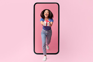 Joyful Korean Woman Giving Present From Big Smartphone, Pink Background, a Photo by Prostock-Studio