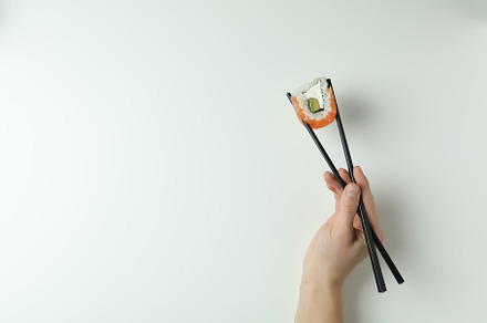 Female hand holding roll with chopsticks on white background, a Food & Drink Photo by AtlasStudio PRO