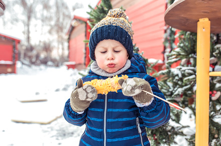 A little baby boy is eating boiled containing corn, hot, and eats