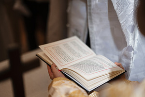 Priest holding an open liturgical book during a church service with ornate vest, a Photo by AS photostudio
