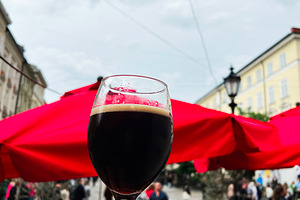 A hand holding a glass of dark beer in an outdoor setting, a Photo by AS photostudio