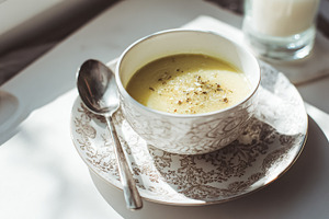 Creamy vegetable soup in ornate bowl, spoon, and candle, creatin, a Photo by Studio ANNA