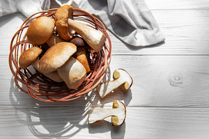Fresh porcini mushrooms in basket on white wooden background, a Food & Drink Photo by Olena Rudo