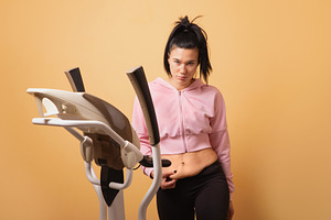 A young woman in sportswear stands by an elliptical trainer and, a Photo by Ales Munt