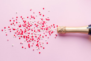 Champagne bottle on pink background containing champagne, hearts, and flat lay